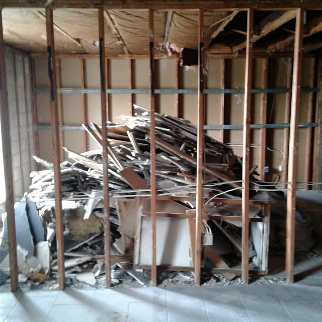Wood and renovation debris inside an interior with exposed wall framing.